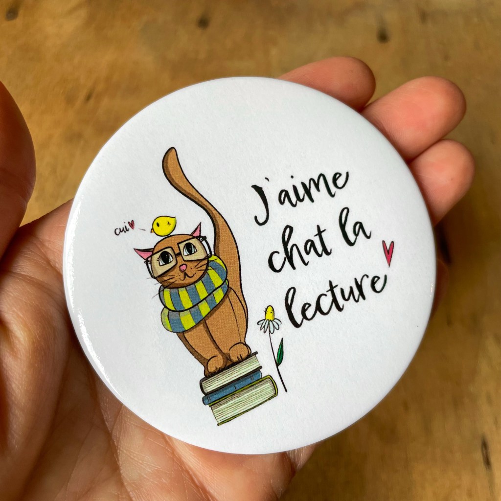 Aimant rond 3 pouces avec un chat à lunettes assis sur des livres avec l'inscription :"J'aime chat la lecture".